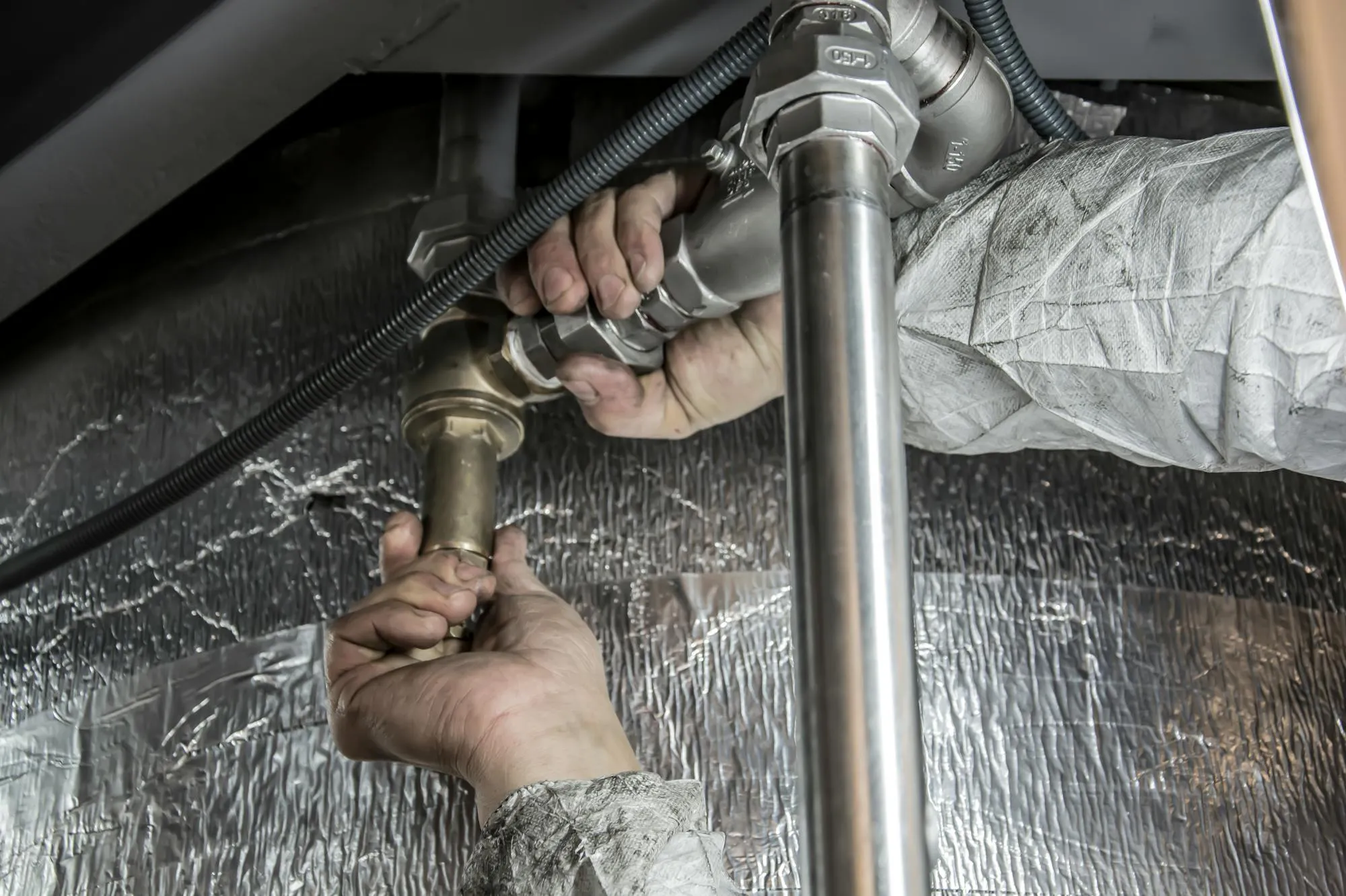 Plumber fitting a brass valve to a stainless pipe under a Birmingham kitchen sink